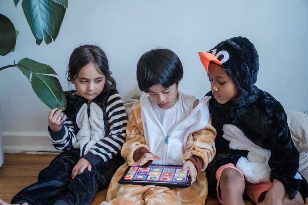 Kids in animal onesies playing on a tablet indoors, enjoying leisure time.